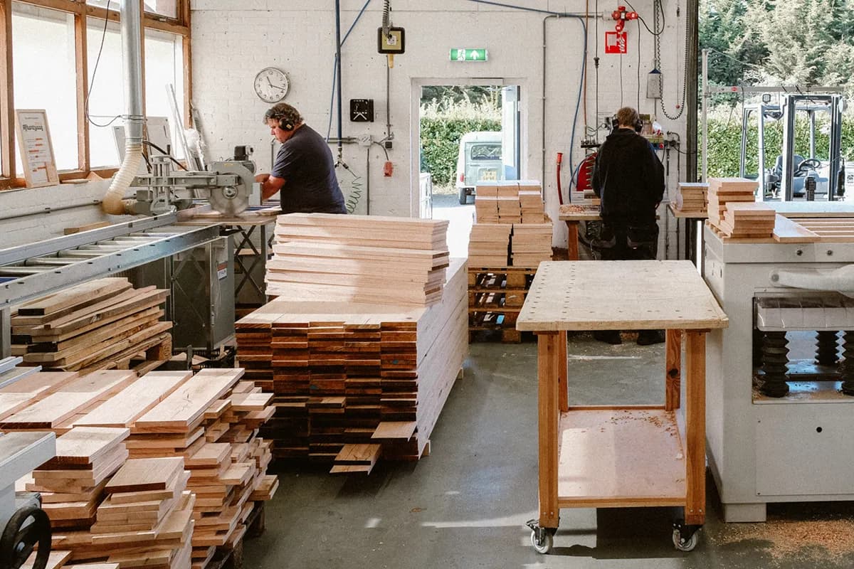 De werkplaats van Binthout: twee medewerkers aan het werk tussen stapels planken.