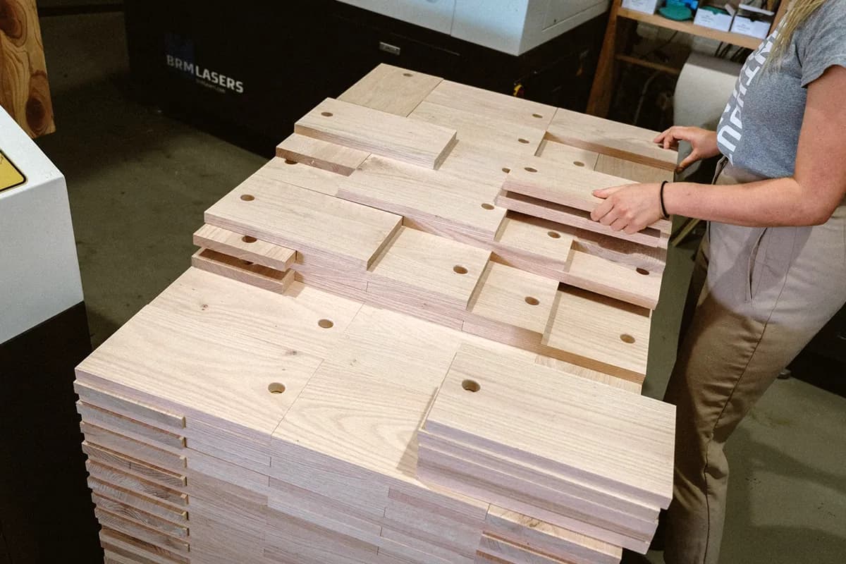 Een medewerker van Binthout bij een grote stapel houten planken met ronde uitsparingen, klaar voor de volgende stap.